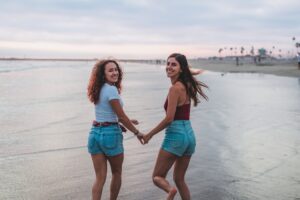two girls running along a beach holding hands