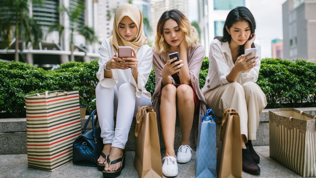 three-women-sitting-looking-at-their-phones-with-shopping-bags